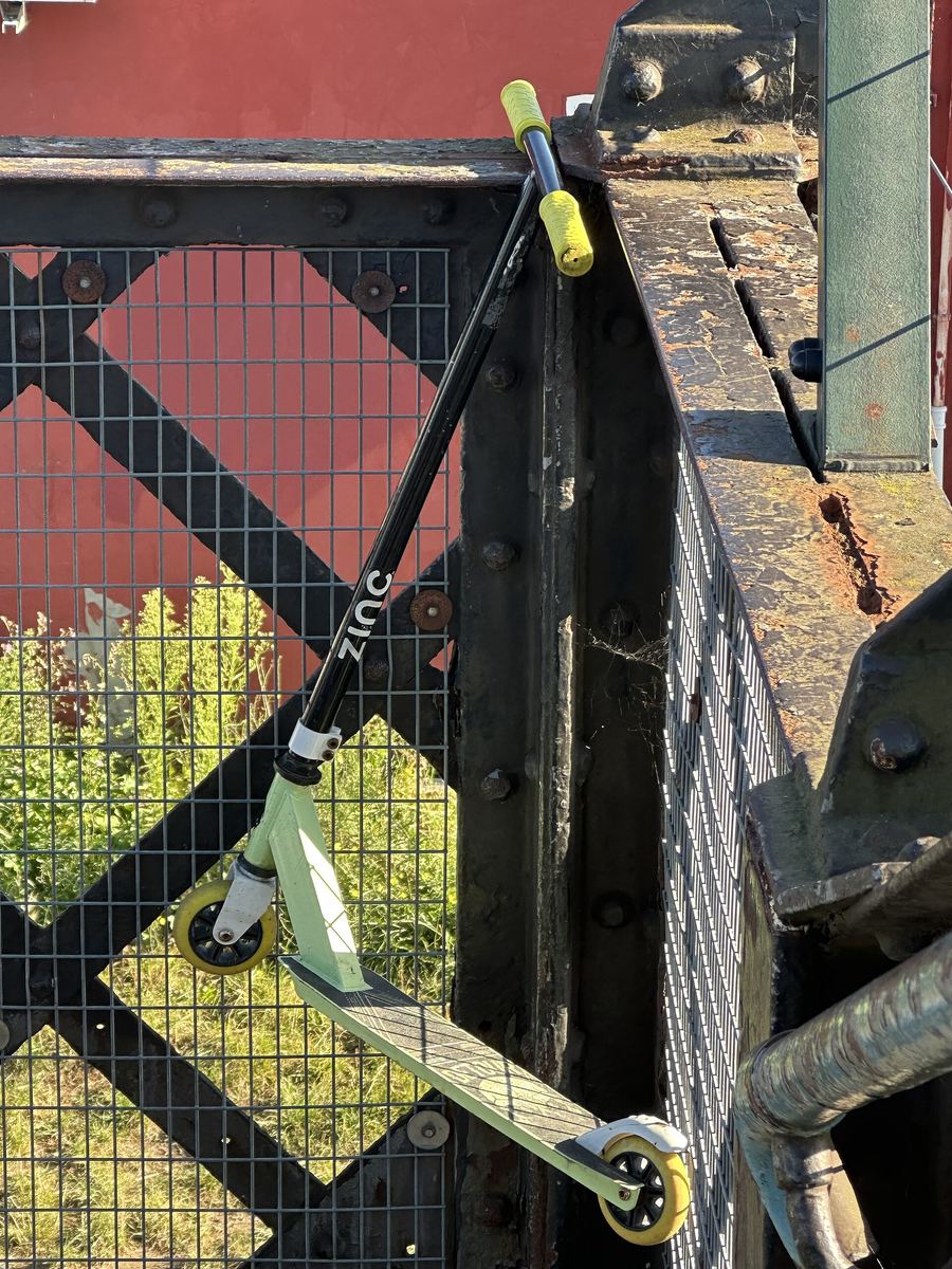 Stunt-Scooter mit hellgrünem Deck und gelben Rollen an ein Geländer gelehnt